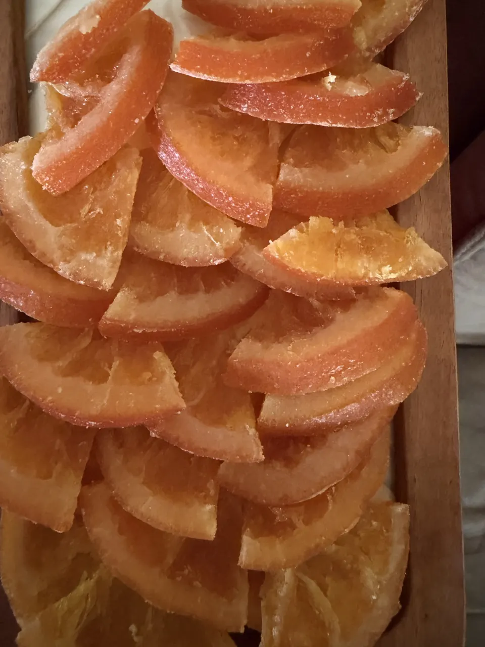 Close-up of glistening candied orange slices stacked in a wooden tray