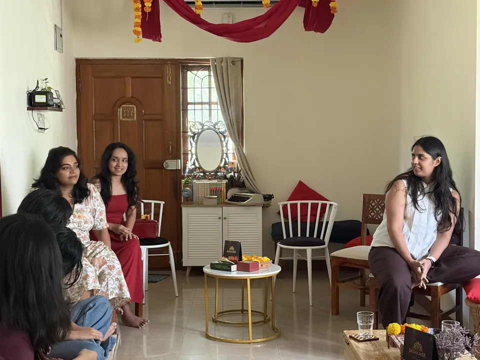 Sunlit living room with maroon drapes and marigold garlands as guests chat around a brass-legged table