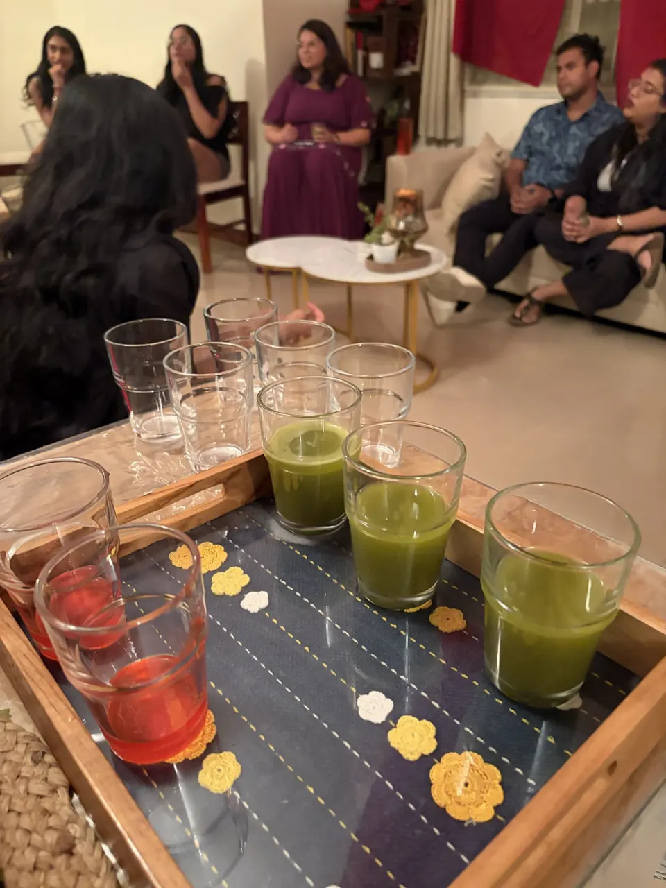 A tray of bright green and ruby red welcome drinks on a navy cloth dotted with crocheted yellow flowers