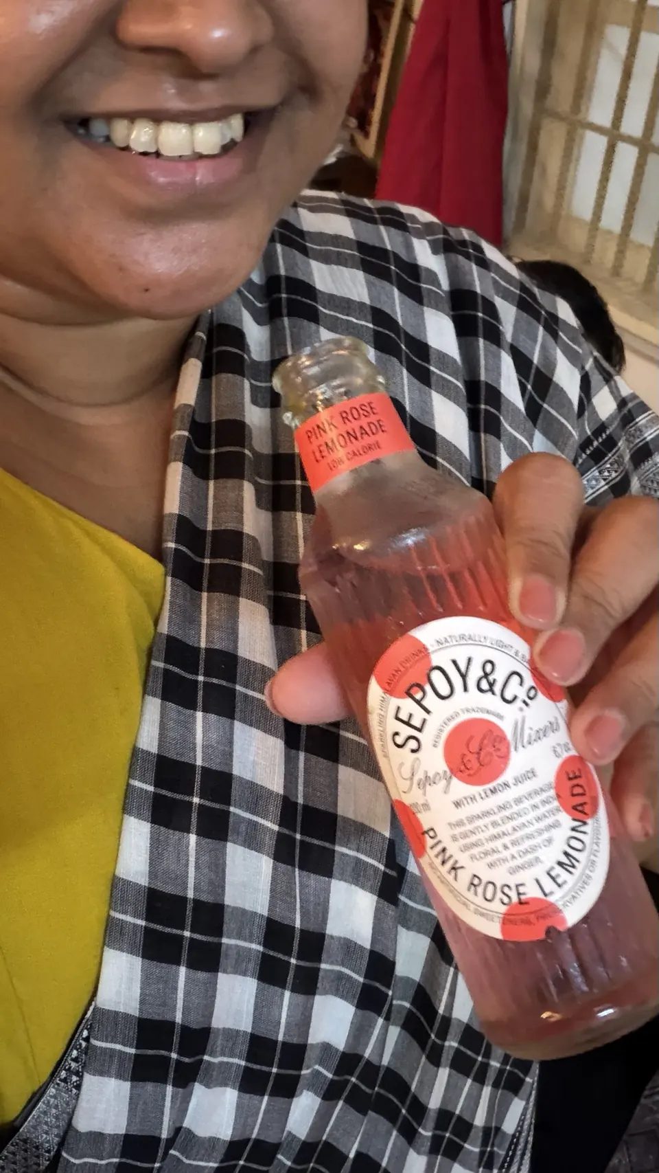 A smiling guest holding a bottle of Sepoy & Co. pink rose lemonade