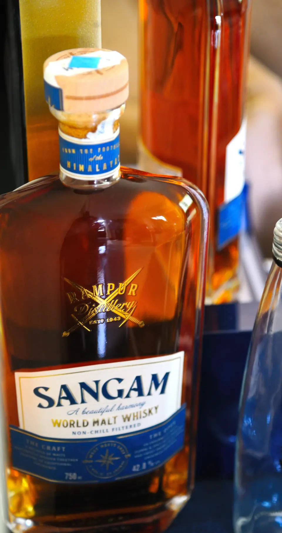 A bottle of Sangam World Malt Whisky from Rampur Distillery glowing amber on the bar