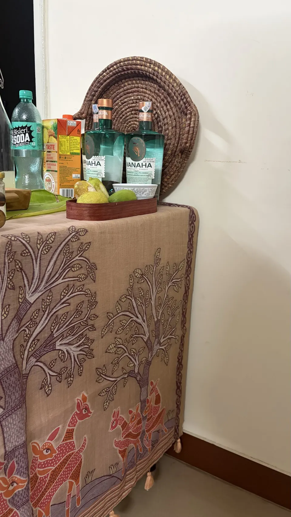 A side table dressed in printed cloth with bottles of Vanaha forest gin, soda and a bowl of limes