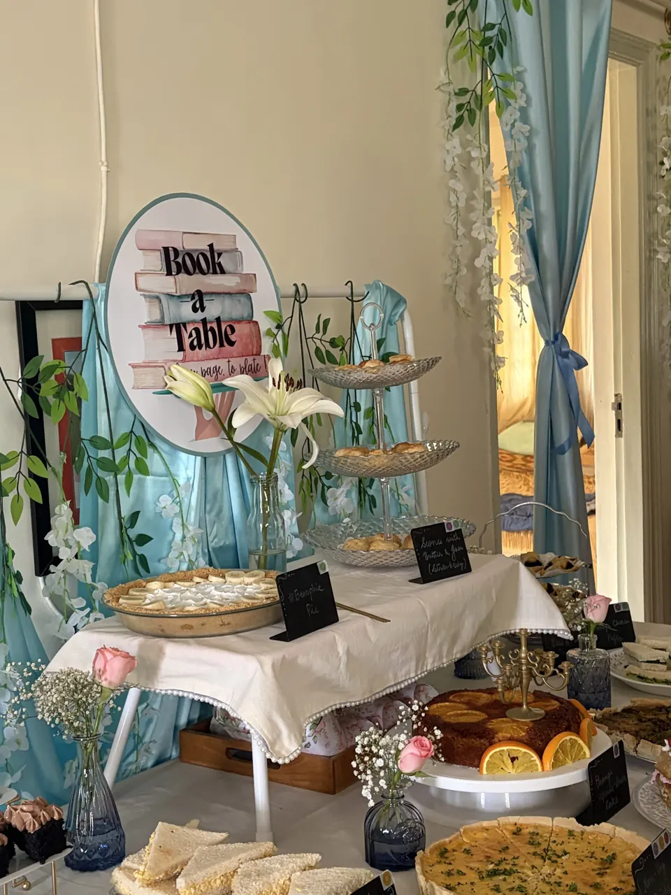 Regency tea table with Book a Table sign, lilies, tiered scone stand, banoffee pie and orange upside-down cake