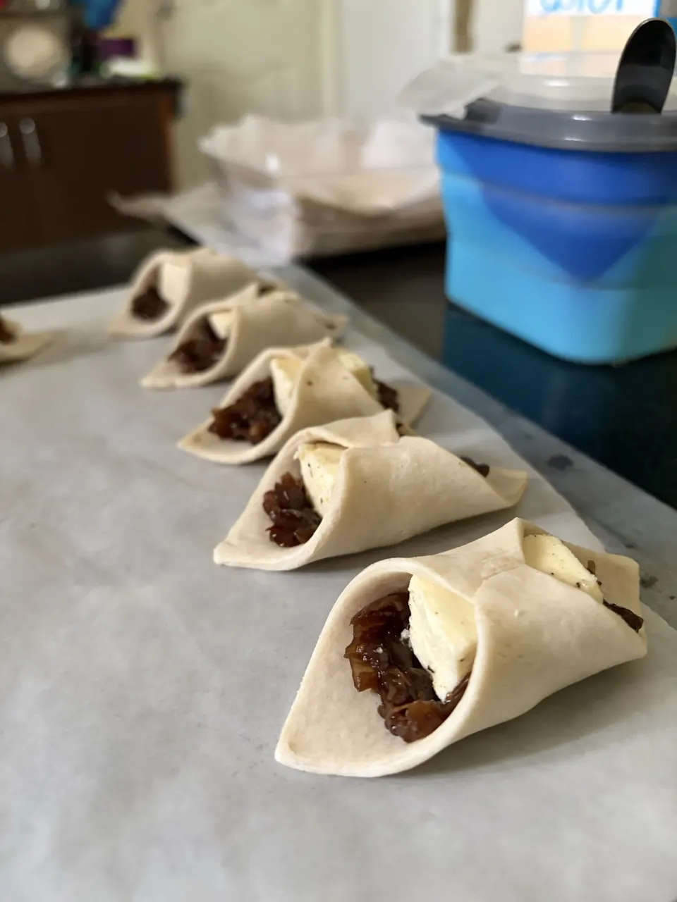 Row of hand-folded pastry parcels filled with caramelised onion and cheese, ready for the oven