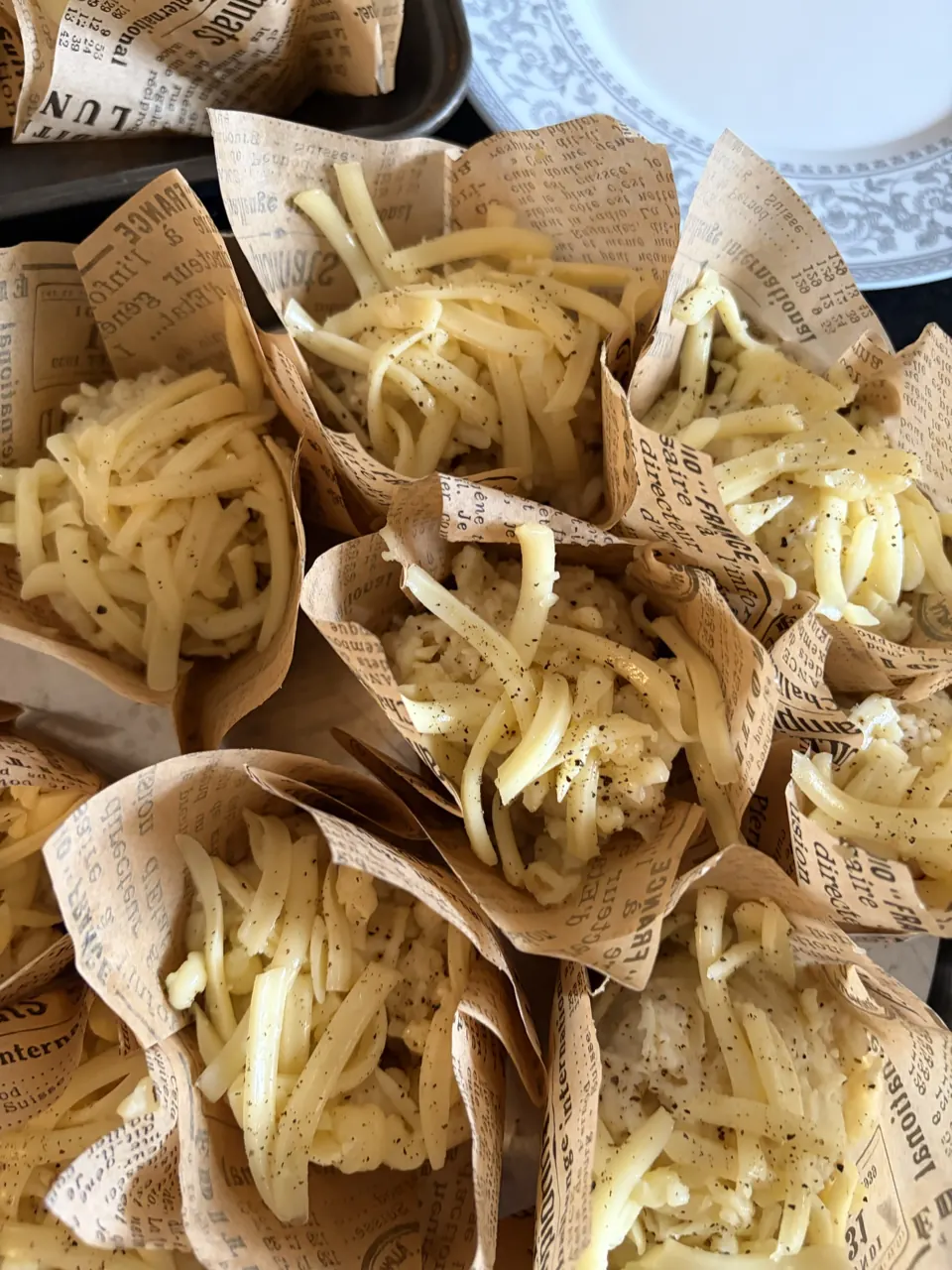 Overhead view of cheesy, peppered macaroni served in vintage newspaper-print paper cups