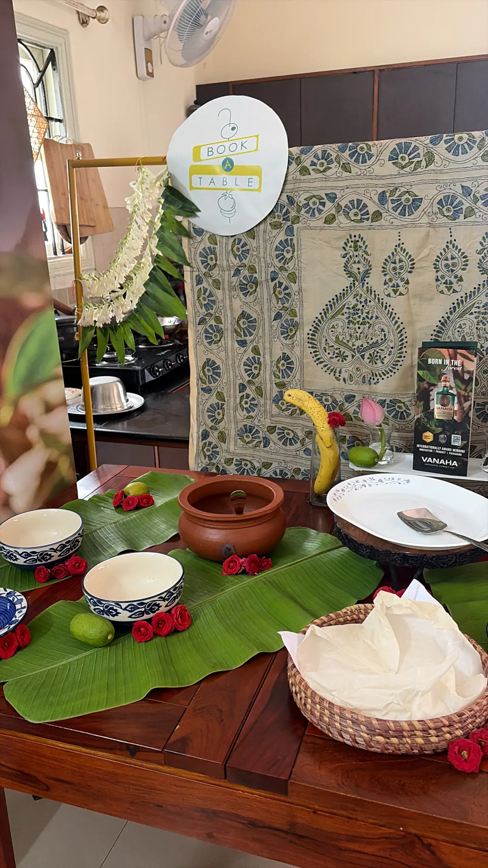 Banana-leaf table with terracotta pot, blue-and-white bowls, roses, jasmine garland and Book A Table sign