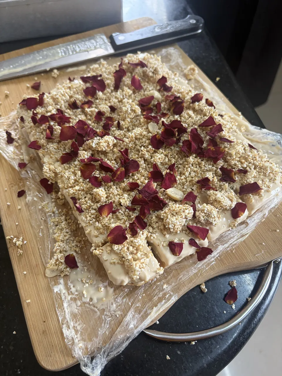 Mishti doi cheesecake slab topped with crunchy crumble and dried rose petals on a board