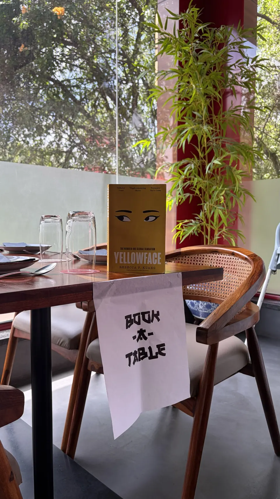 Yellow Yellowface paperback by R.F. Kuang standing on a wooden table beside a hand-lettered Book-A-Table sign