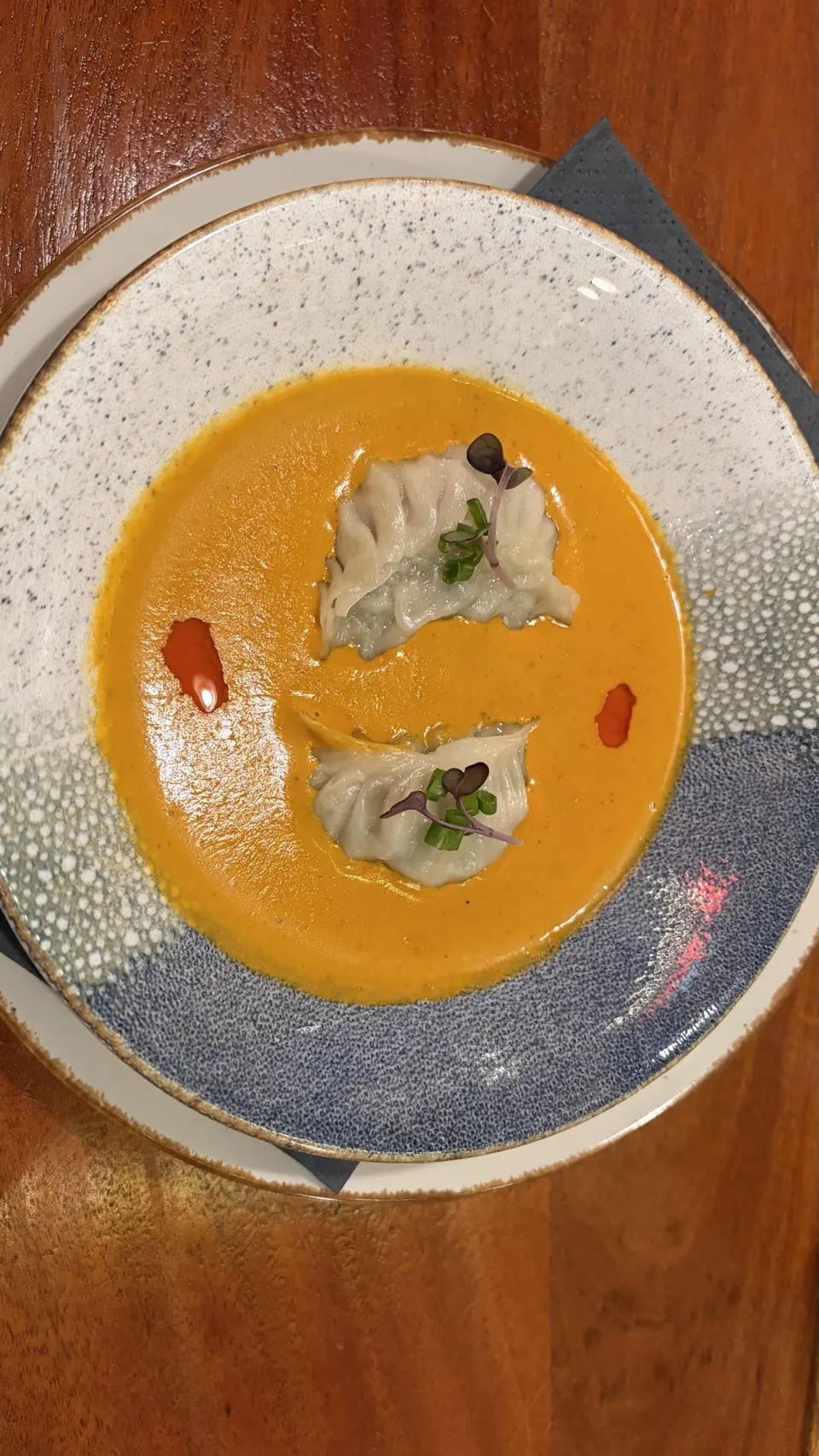 Two delicate dumplings in a vivid orange broth with microgreens on a speckled blue plate