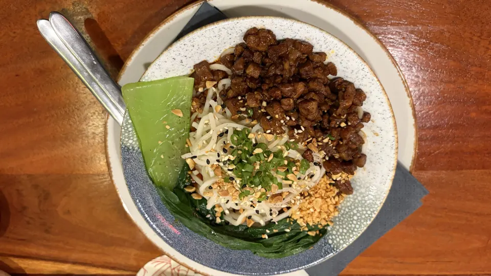 Bowl of wheat noodles topped with crumbled savoury mince, peanuts, sesame, spring onion and bok choy