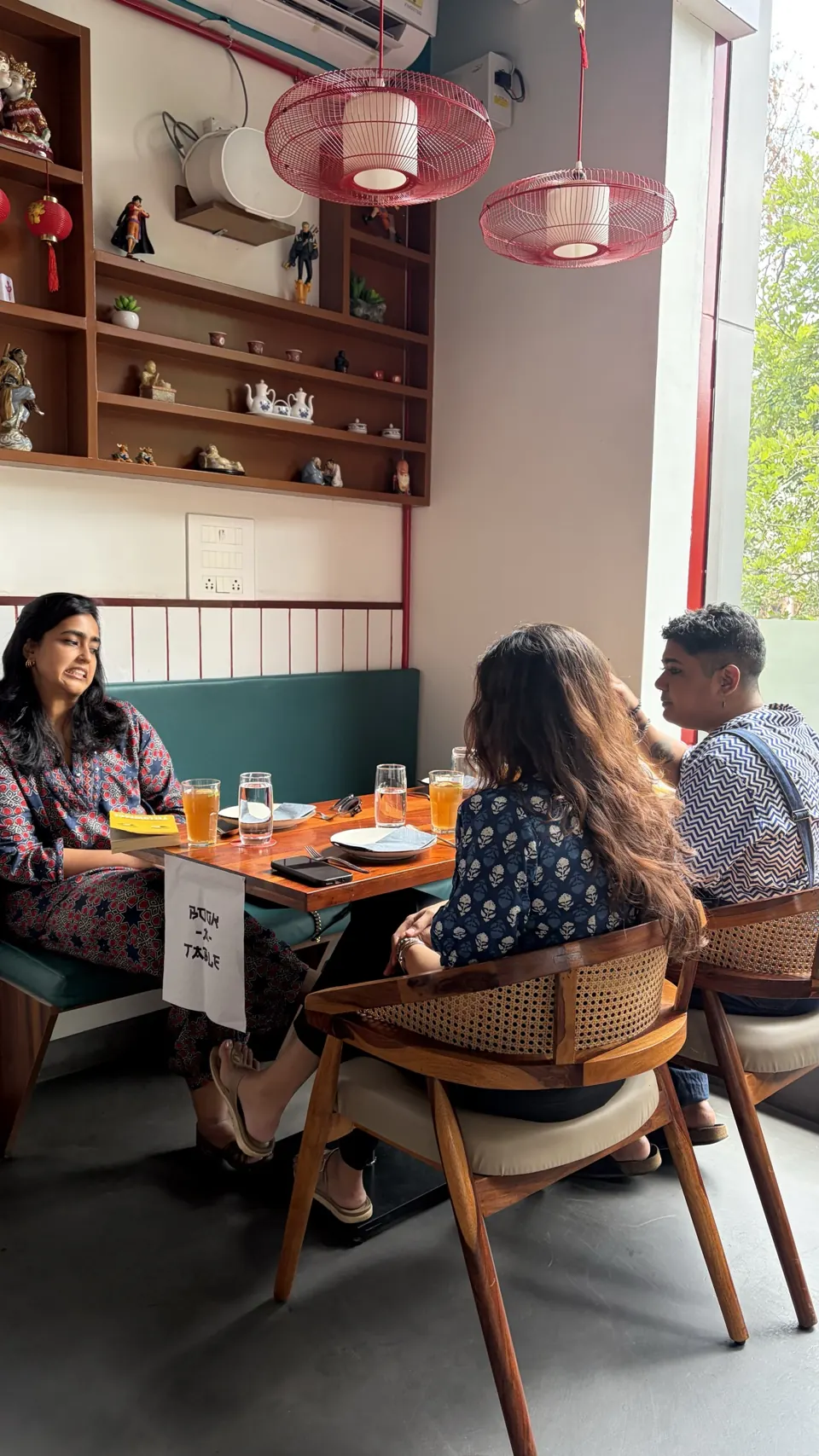 Guests chatting over iced tea at a teal banquette under red wire pendant lamps